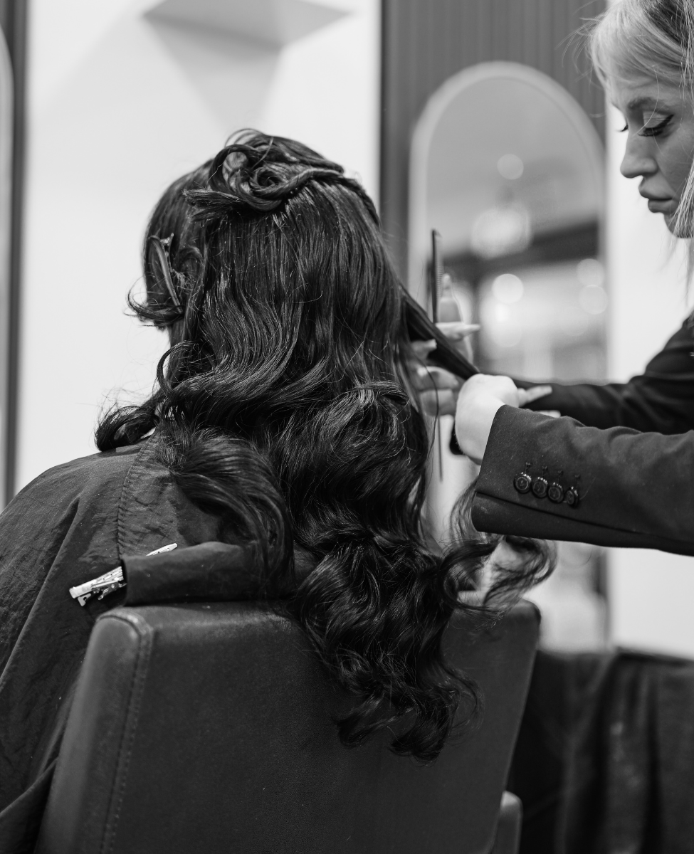 black and white picture of hair salon hair cut one woman with long black hair sitting in chair and other one with blond hair cutting her hair
