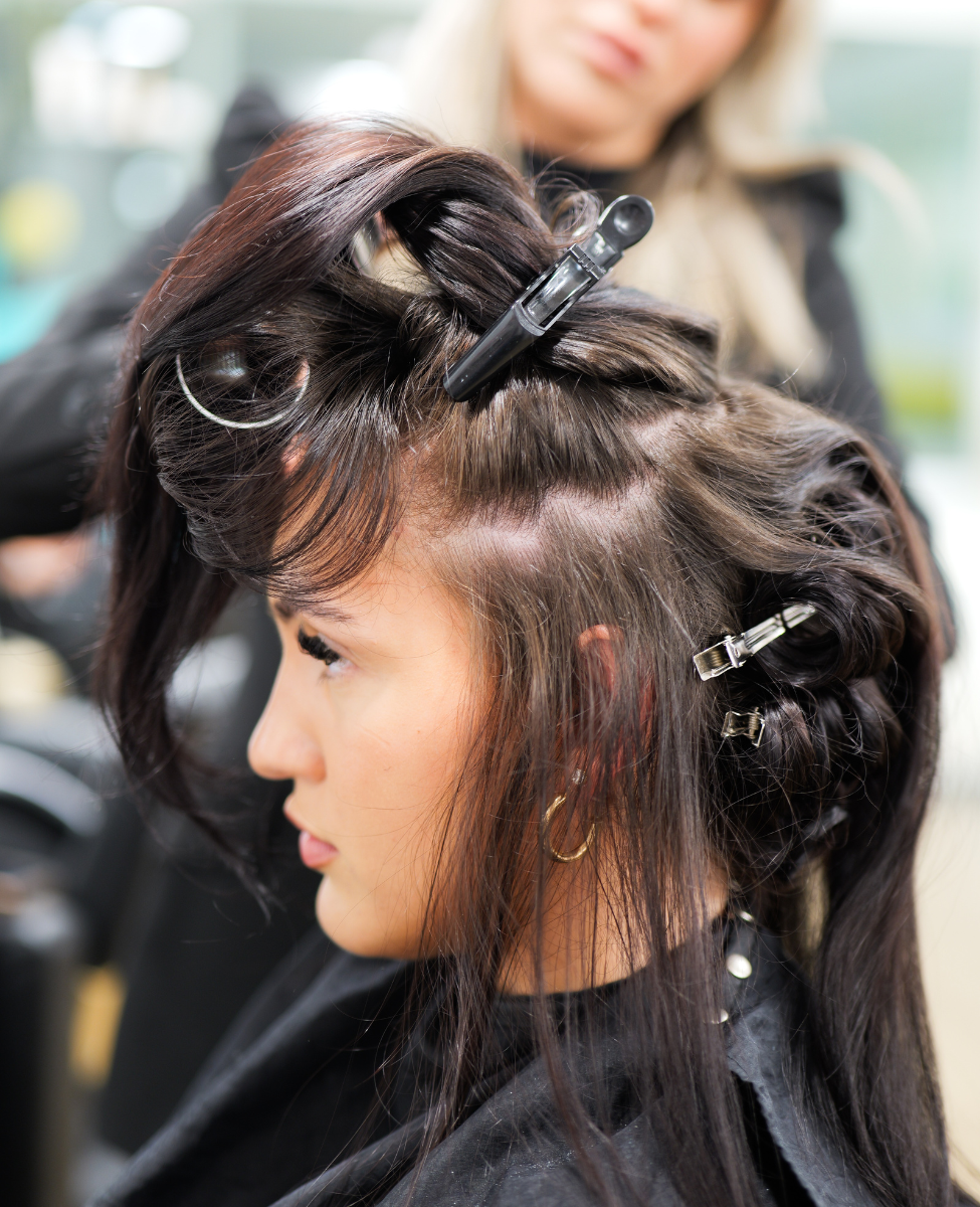 close up of young women sitting in hair dresser chair having her black hair styled with a lot of hair accessories