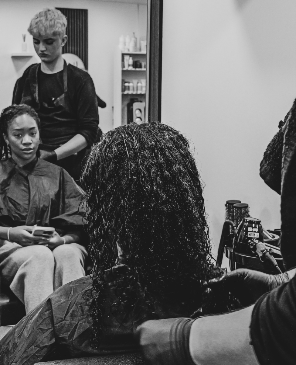black and white image of a beautiful young black woman with short curly hair having her hair styled by a junior stylist in best hair salon in sheffield