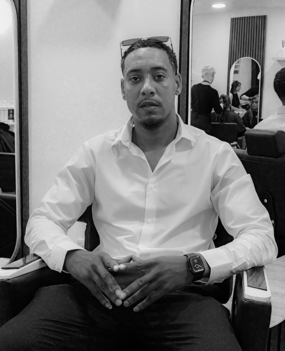 black and white image of young male with sunglasses on his head and white shirts and black trousers sitting on high chair in The Style Lounge No. 1 sheffield