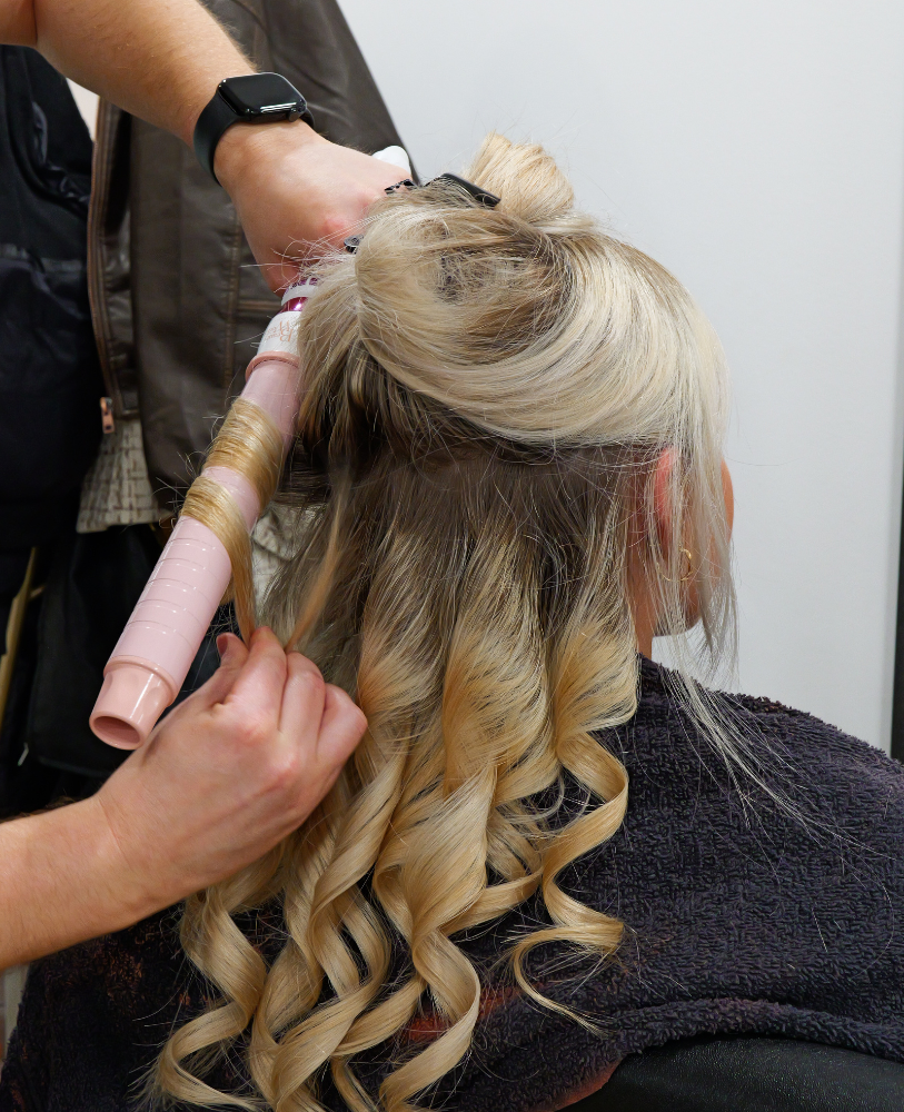 young blond woman is getting her hair restyled and curled by pink hair curler in luxury hair salon in sheffield