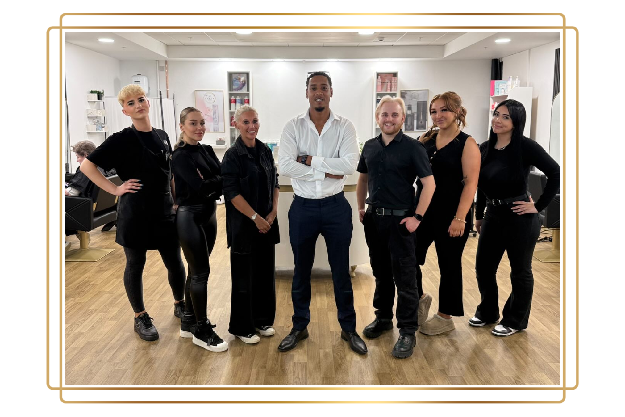 team of hair stylists six of them wearing black uniforms and the owner in middle young man wearing white shirts and black trousers
